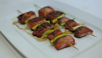 In the Cooking Demonstration, skewers of grilled meat paired with green vegetables are elegantly displayed on a rectangular white plate, enhanced by a delicious sauce and slightly charred to perfection for a savory look.